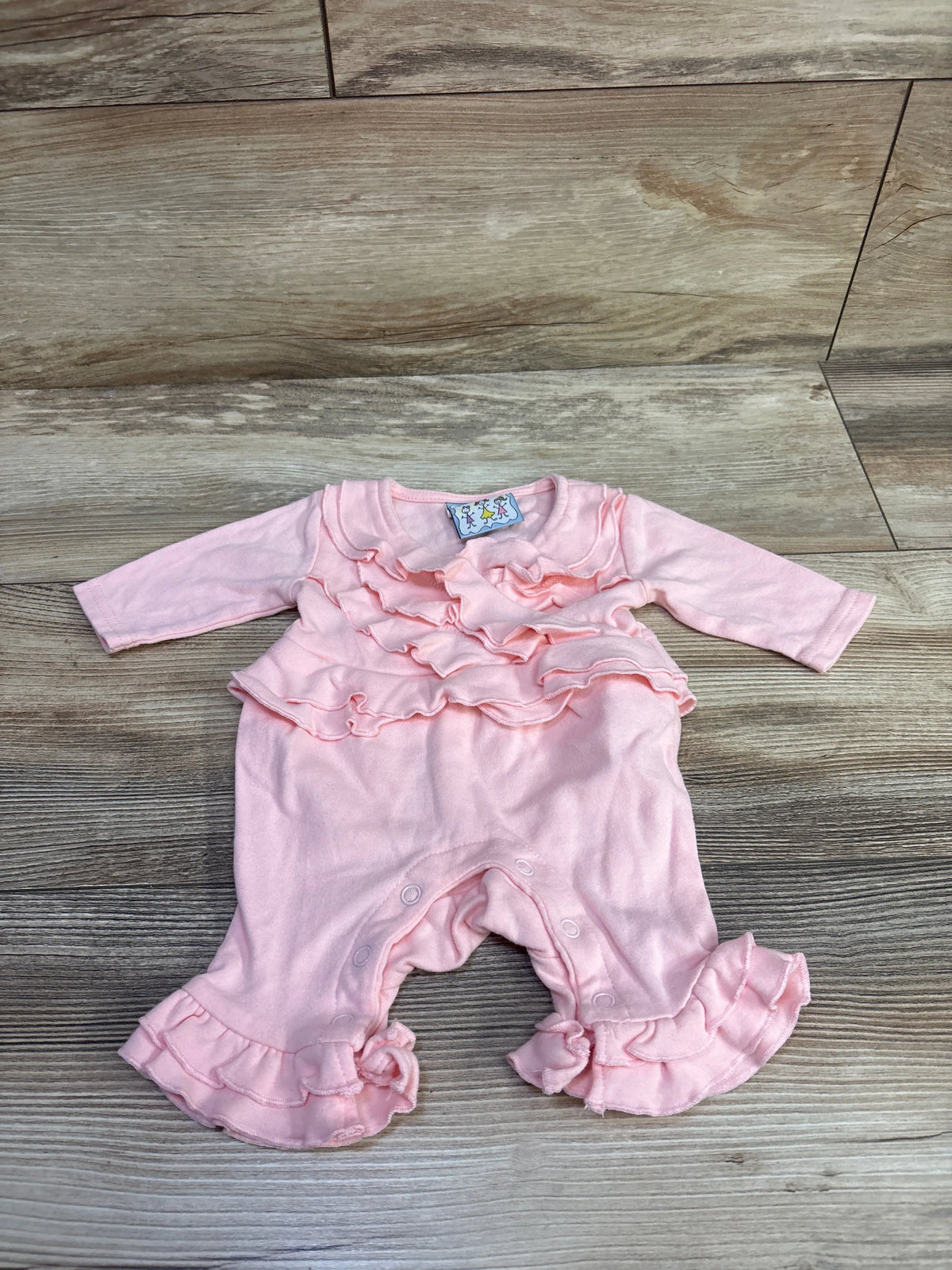 Front view of Three Sisters ruffle coverall in pink, showcasing layered ruffles and ruffled cuffs on a wood-look floor