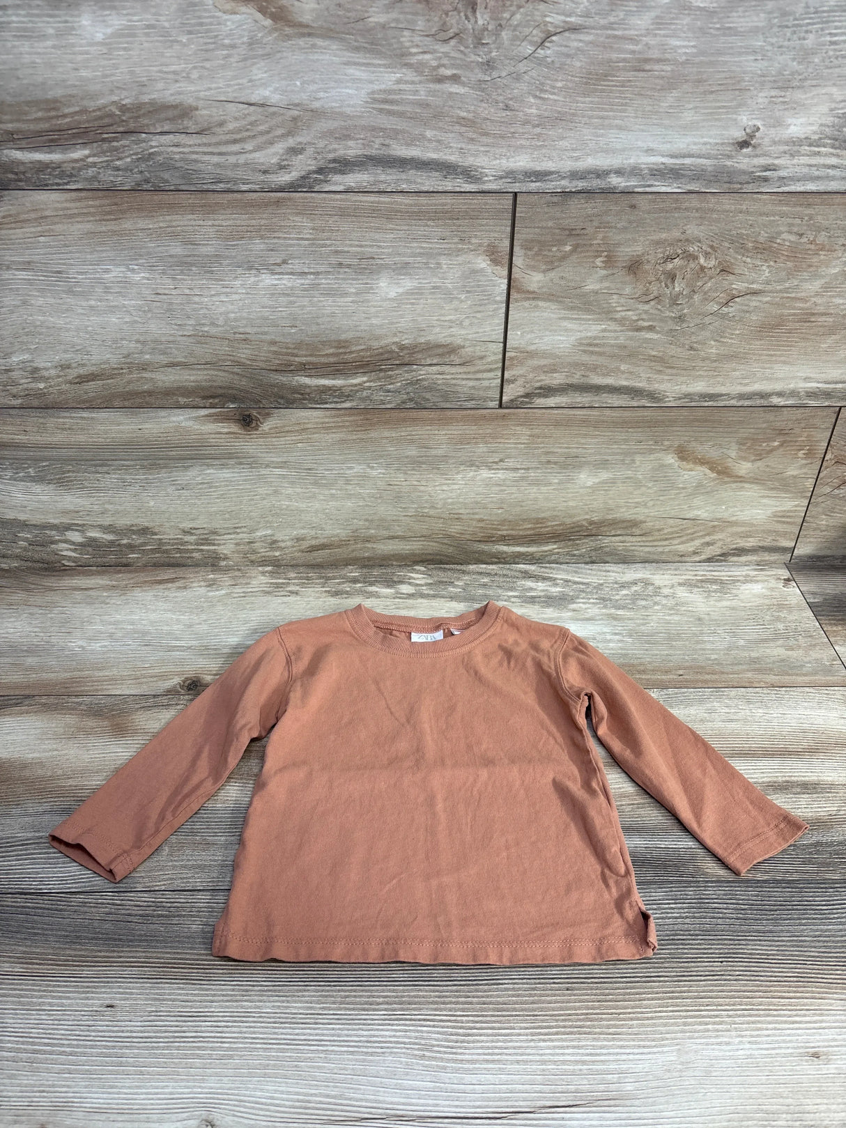 Rust-colored long-sleeve toddler shirt on wooden background, children's resale clothing