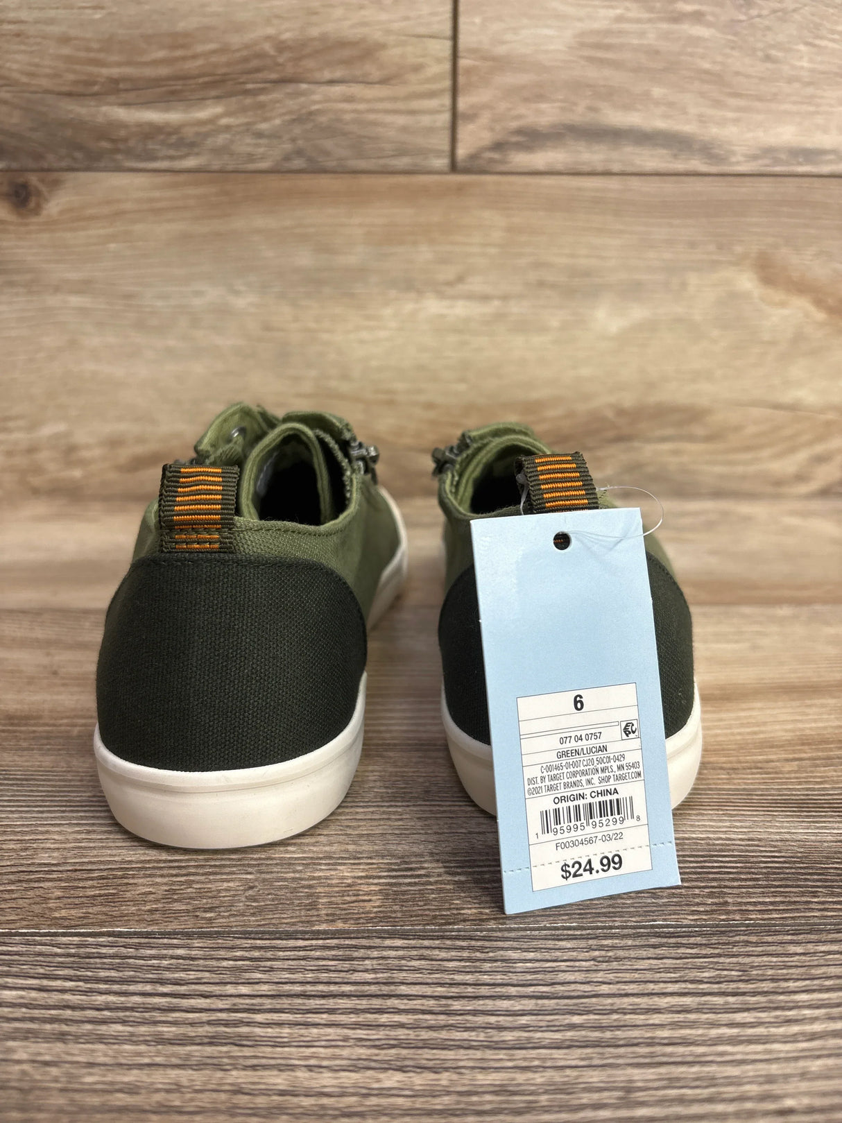 Back view of green and black toddler sneakers with orange striped pull tabs and $24.99 price tag on wood surface