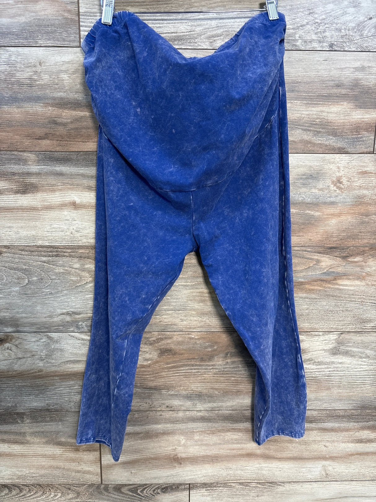Blue acid-wash style hooded sweatpants hanging on clips against wooden wall background