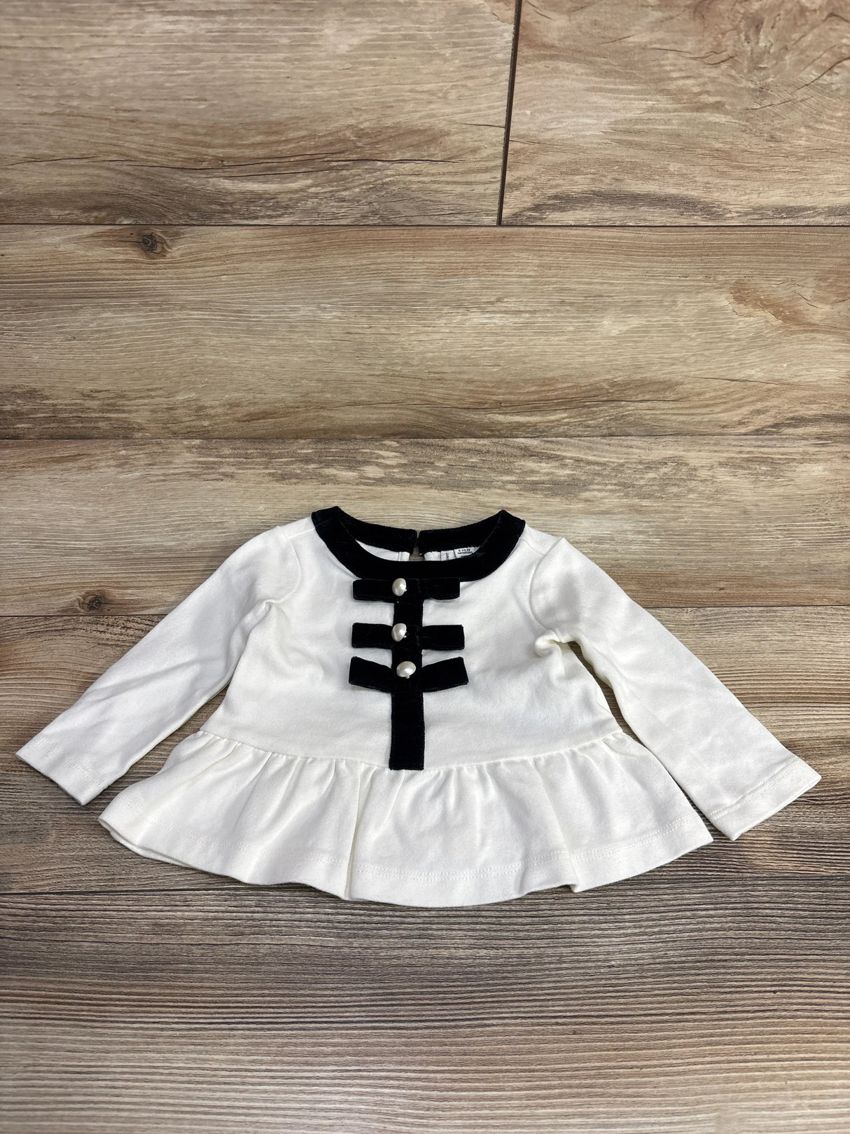 Flat lay of cream velvet peplum top (Janie & Jack, 3-6 months) showcasing front bow, pearl buttons, ruffled hem on wood floor