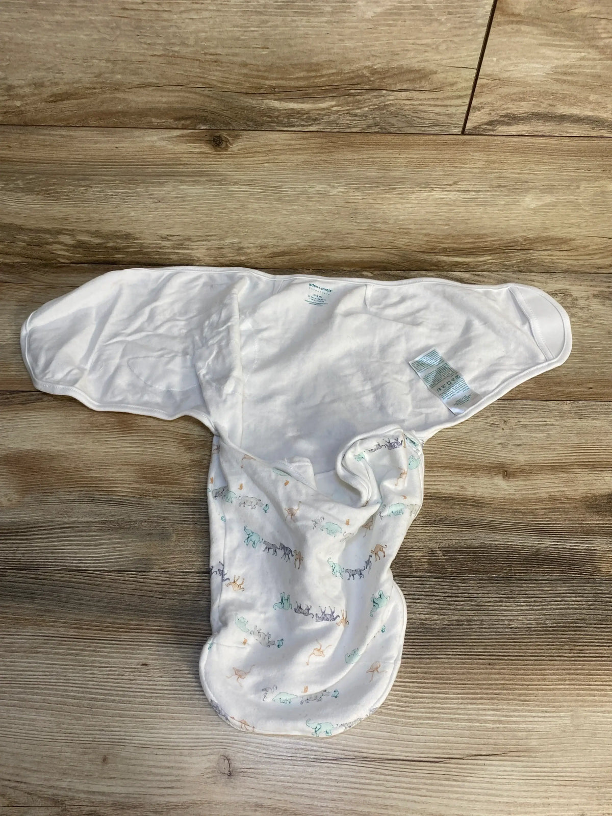 White baby swaddle sack with pastel animal print laid flat on wooden surface