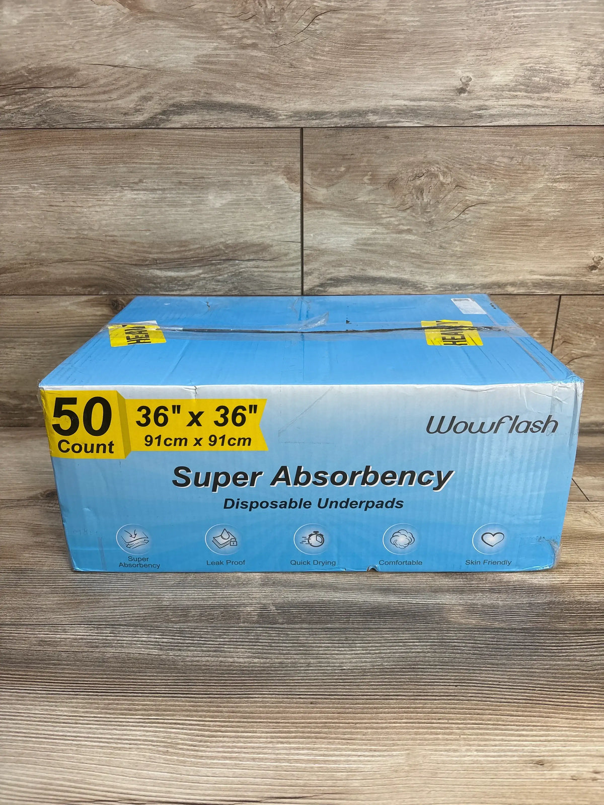 Front view of Wowflash disposable underpads box showing 'Super Absorbency', 50 count and 36 x 36 in (91 x 91 cm) size on wood background