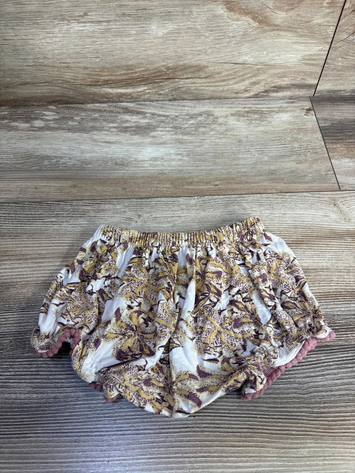 Front view of yellow bamboo pom-pom bloomers showcasing the elastic waistband and pom-pom trim on a wood-look floor