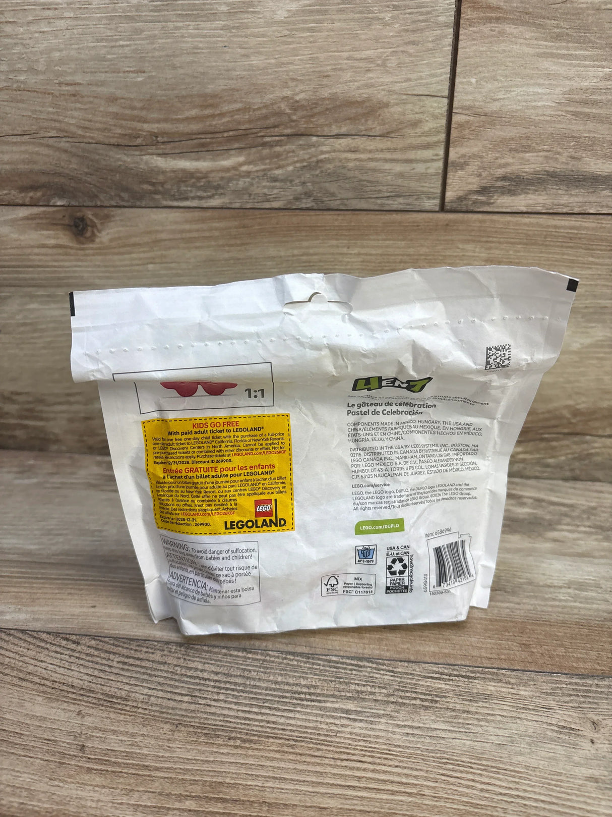 Rear view of sealed LEGO DUPLO Celebration Cake bag showing back panel and yellow KIDS GO FREE promo label on wood floor