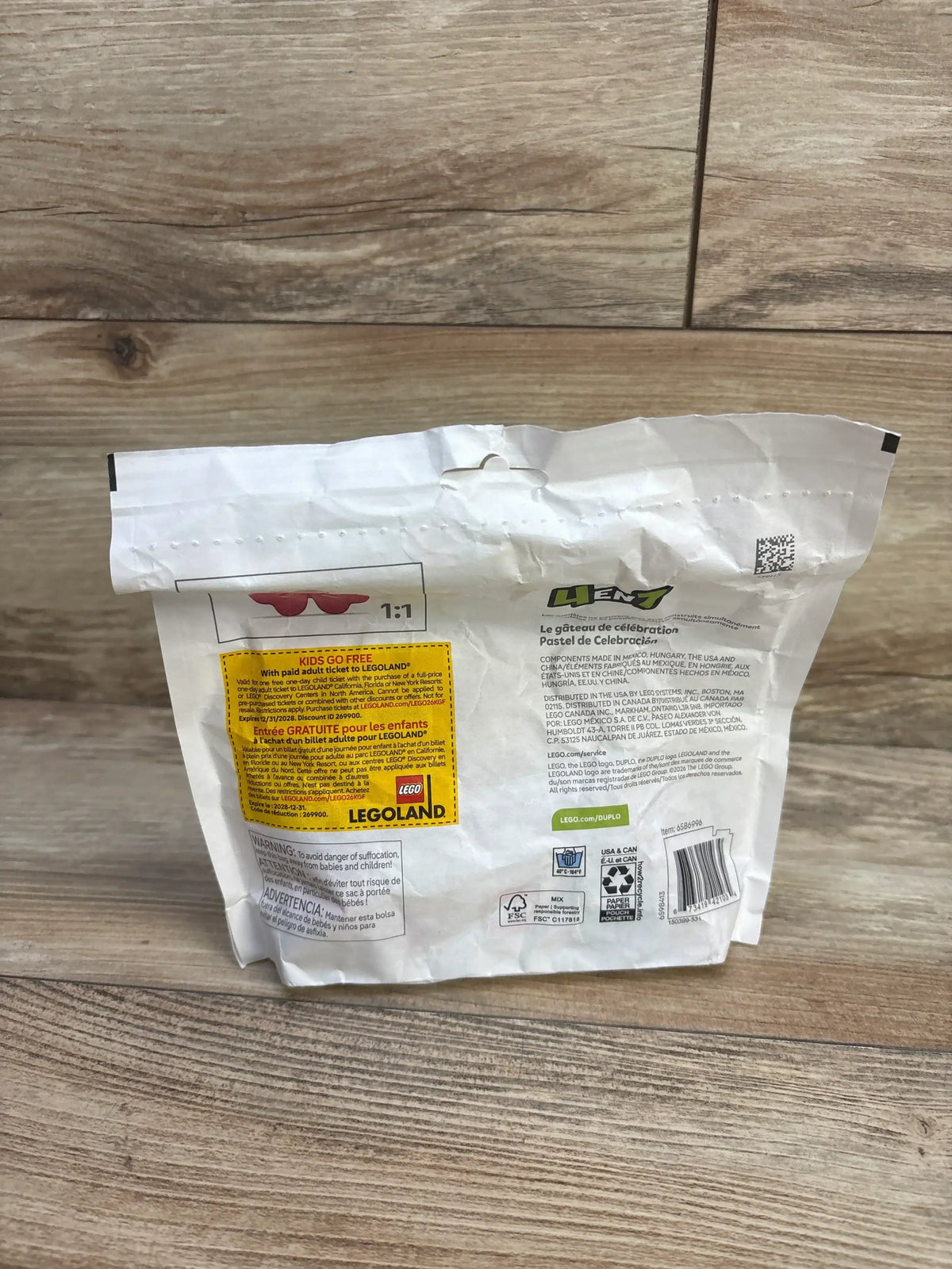 Rear view of sealed LEGO DUPLO Celebration Cake bag showing back panel and yellow KIDS GO FREE promo label on wood floor