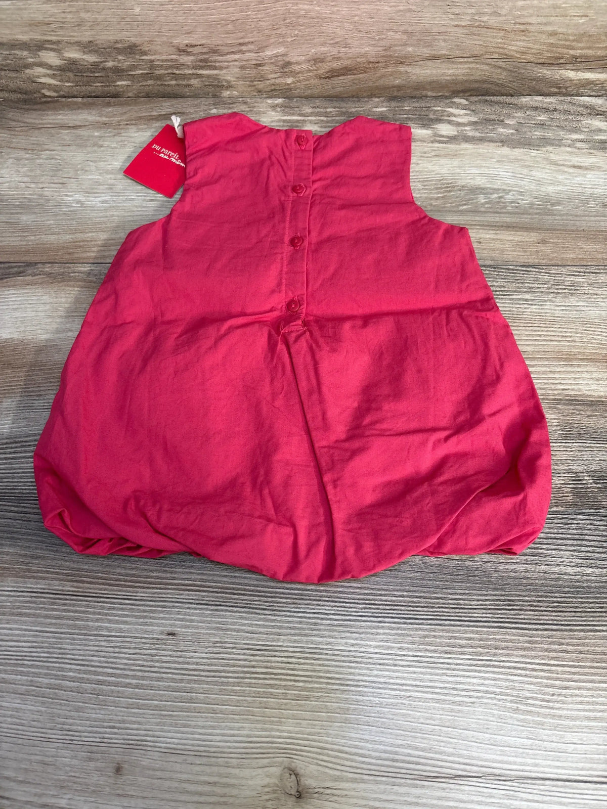 Back view of pink baby bouffant dress 3-6 months showing button-back closure and gathered bubble hem on wood surface