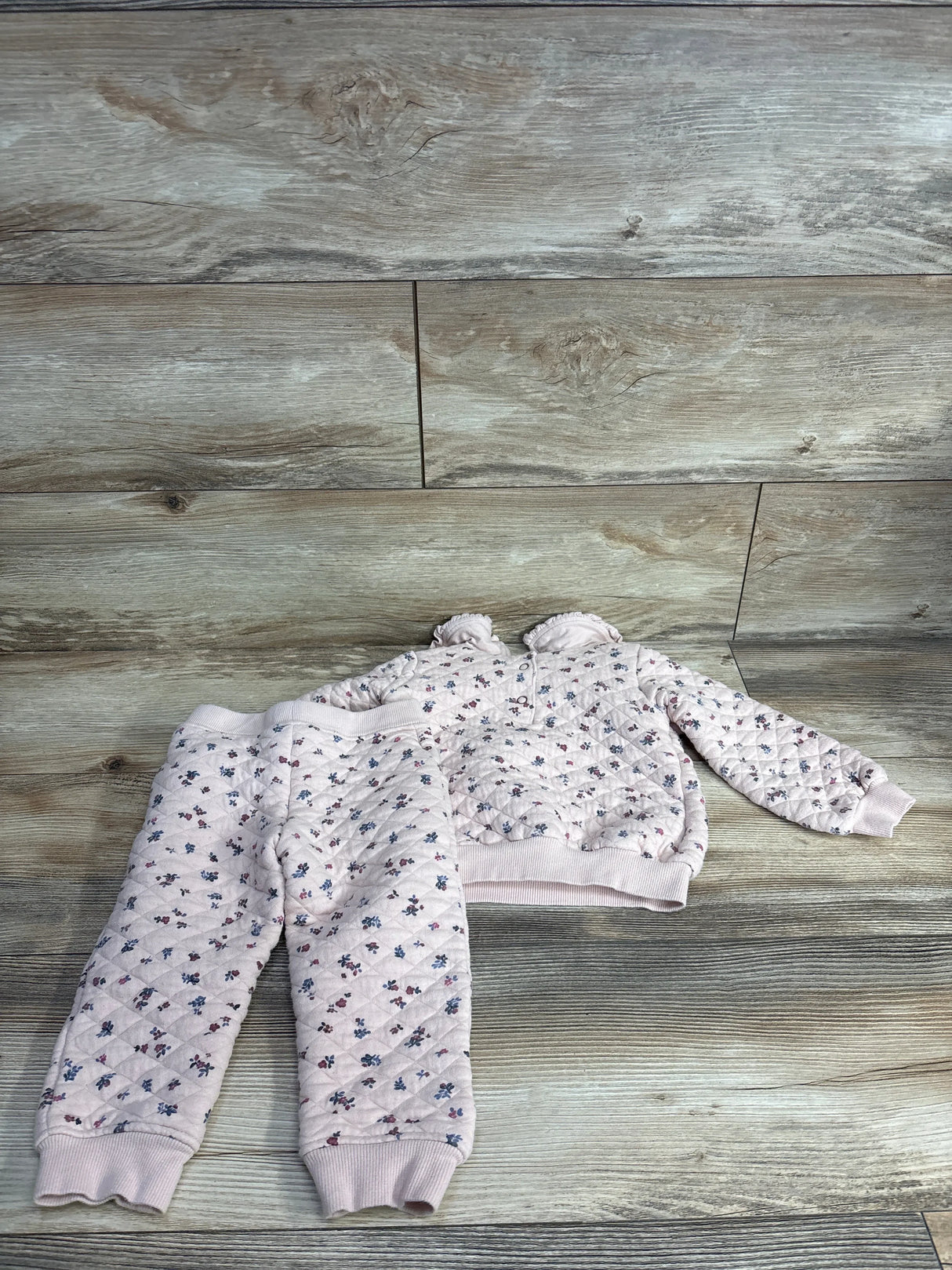 Quilted pink floral toddler pajama set with pants and sweatshirt on wooden floor