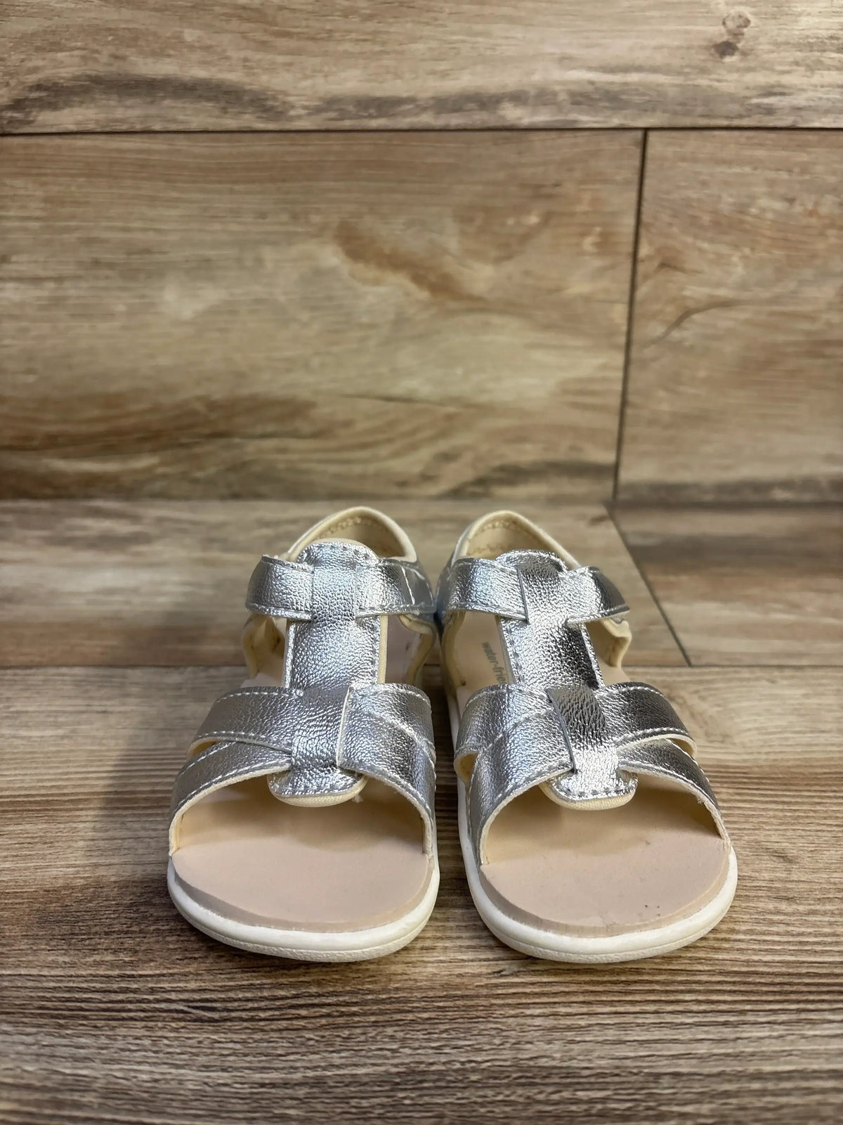 Front view of See Kai Run Shayna sandals in silver metallic, showcasing strappy uppers and adjustable straps on wood
