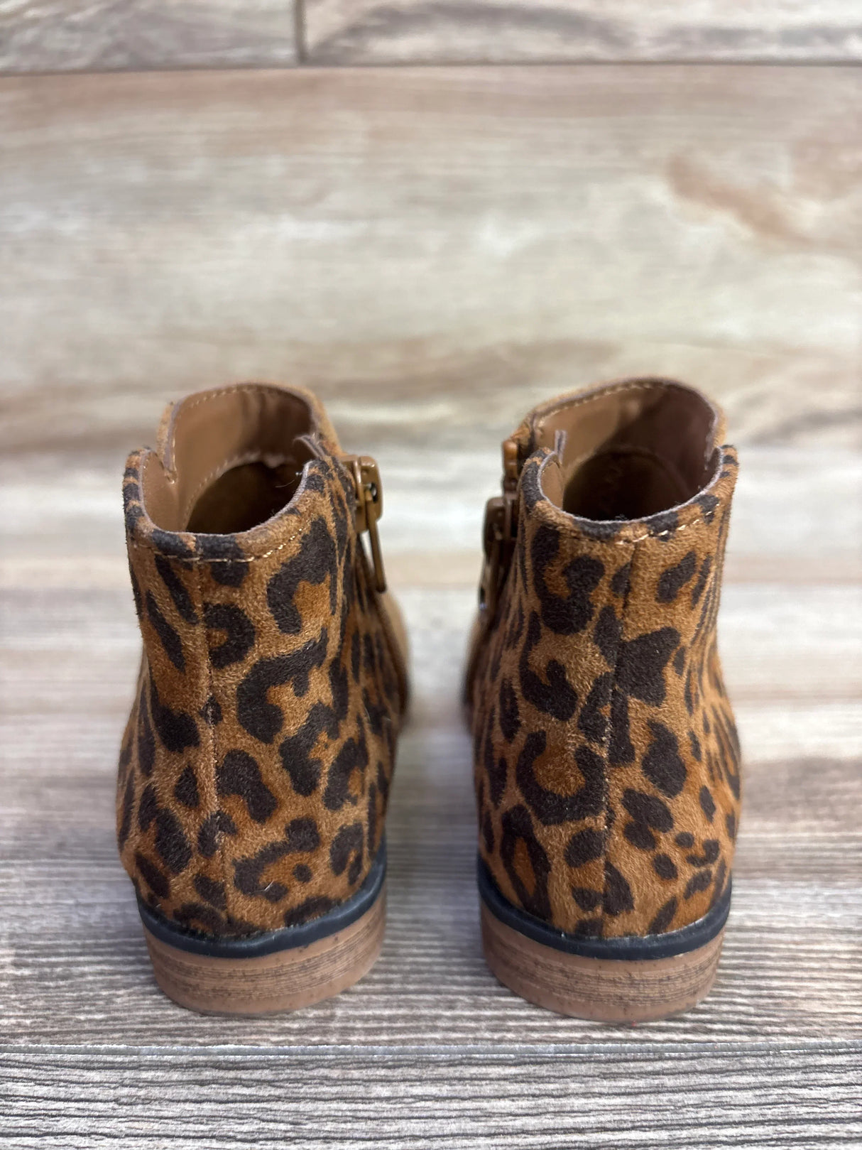 Back view of toddler leopard print ankle boots with side zippers on wooden floor