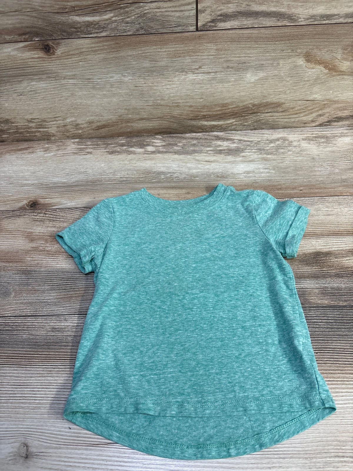 Front flat-lay of green heathered Cat & Jack toddler T-shirt showing short sleeves and curved high-low hem on wood background