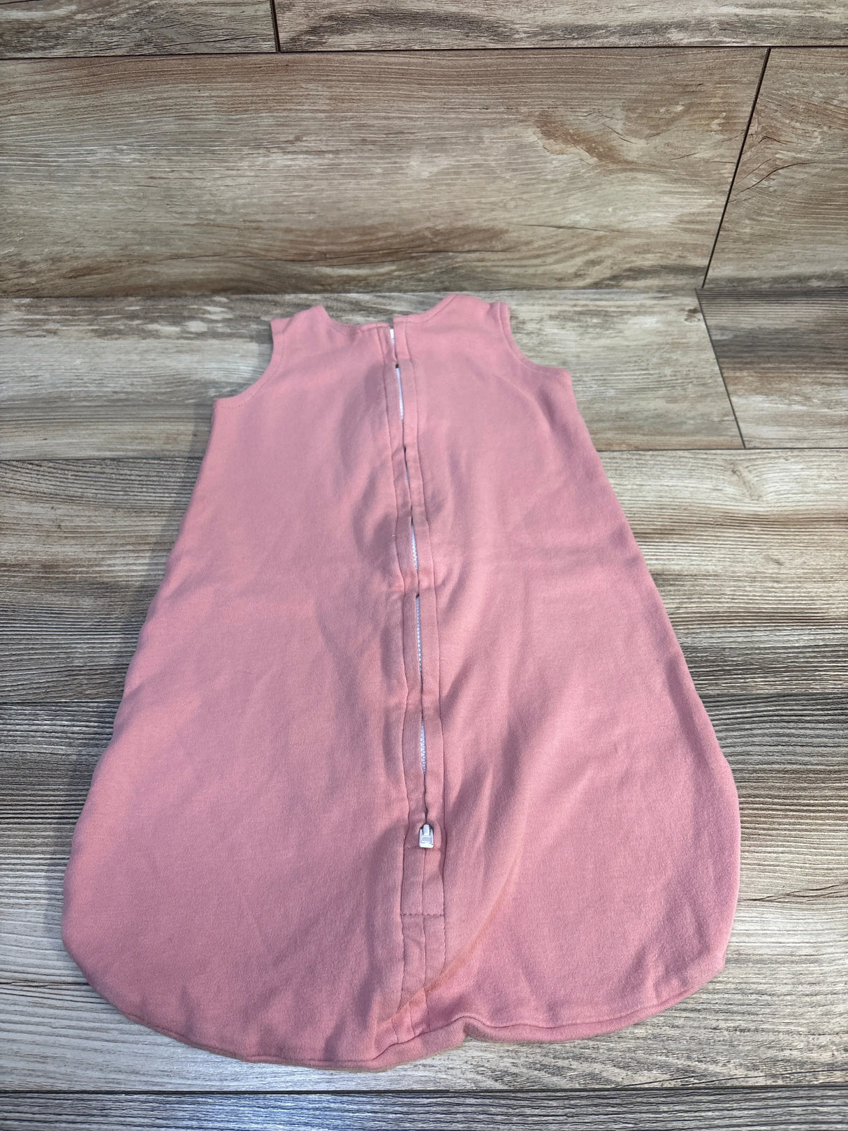 Pink baby sleep sack with front zipper, laid flat on wood floor, ideal for infant bedtime comfort