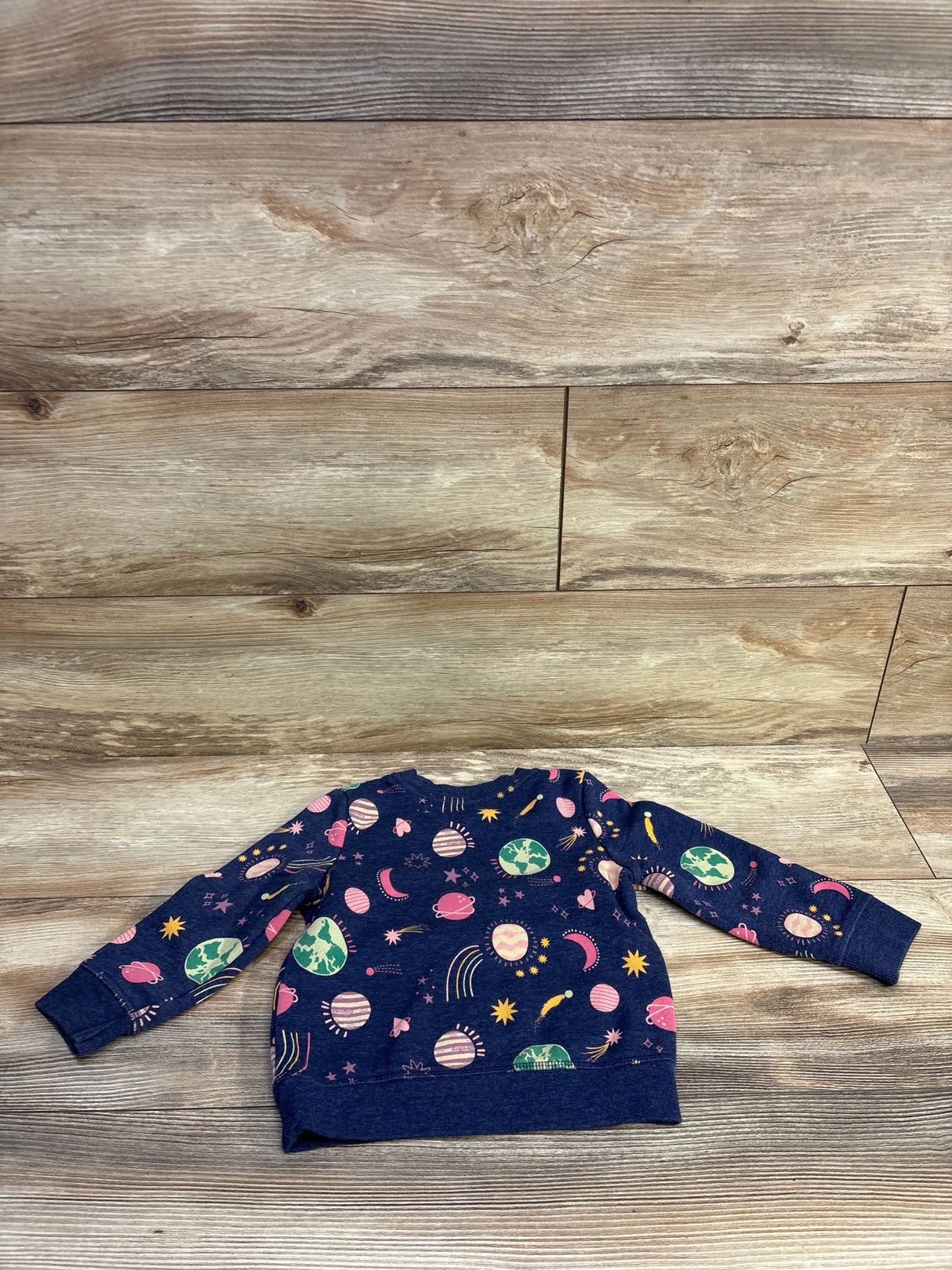 Flat lay of Cat and Jack navy pullover sweatshirt showcasing all-over space print with ribbed cuffs on wood plank background