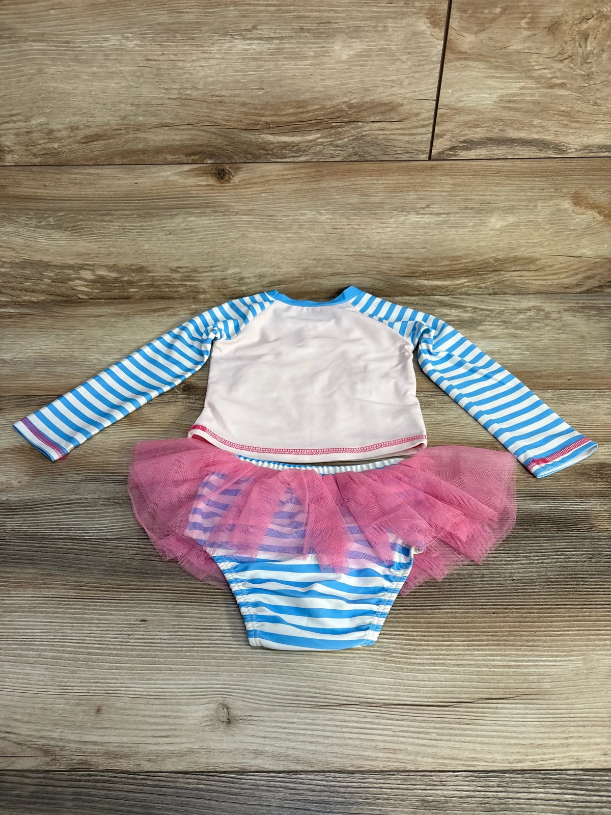 Back view of MudPie 2pc striped rashguard swimsuit set with blue and white stripe rashguard and pink tulle skirt bottoms on wood plank floor