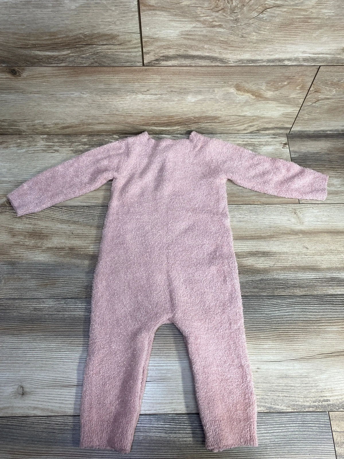 Soft pink fuzzy baby onesie laid flat on wood floor background