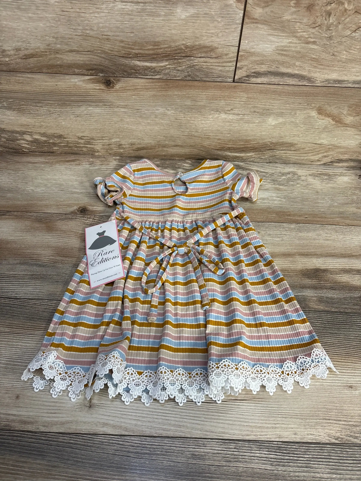 Top-down view of Rare Editions ribbed toddler dress size 2T showcasing pink, blue and mustard stripes, waist tie and white lace hem on wooden floor