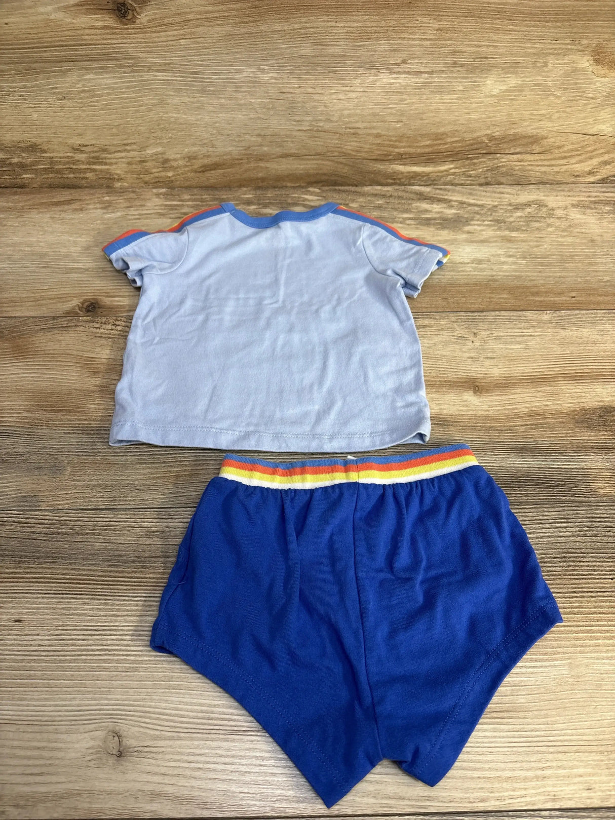 Flat lay of Cat & Jack baby 2-piece: light blue short-sleeve shirt with rainbow trim and royal blue elastic shorts on wood background