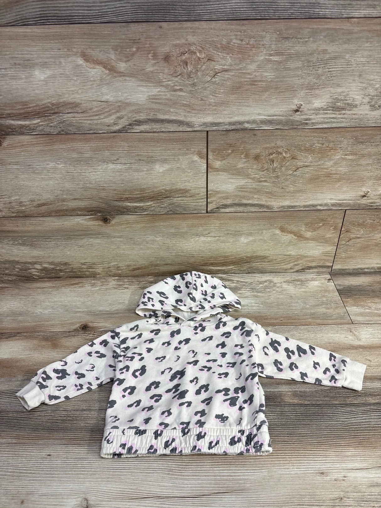 Toddler sized hooded sweatshirt with gray and pink leopard print on a wood floor background