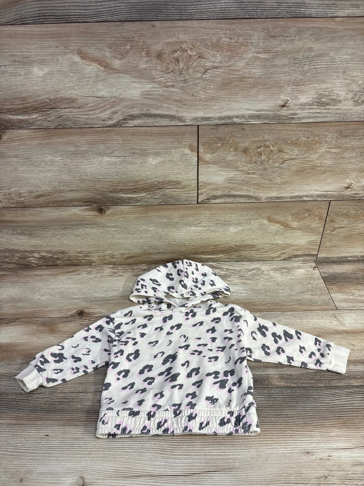 Toddler sized hooded sweatshirt with gray and pink leopard print on a wood floor background
