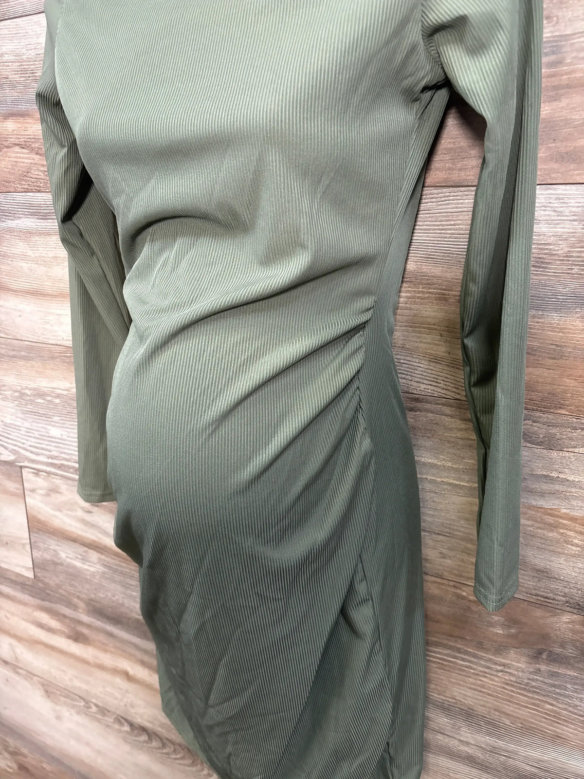 Olive green long sleeve maternity dress with ruched side on wood background