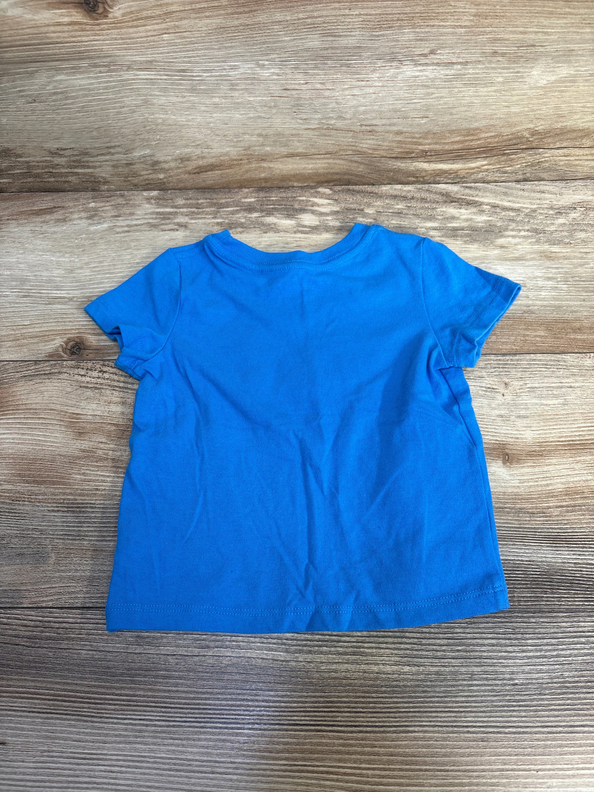 Bright blue short-sleeve toddler t-shirt laid flat on wood surface