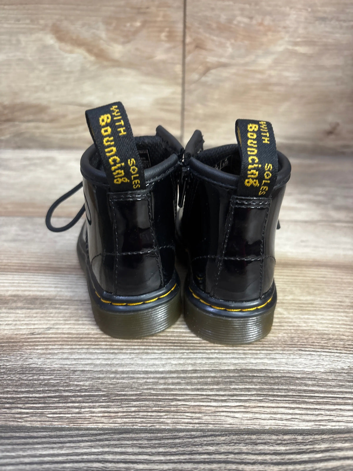 Rear view of Dr. Martens 1460 boots in black, size 4C, showcasing yellow stitching and pull tabs on a wood floor
