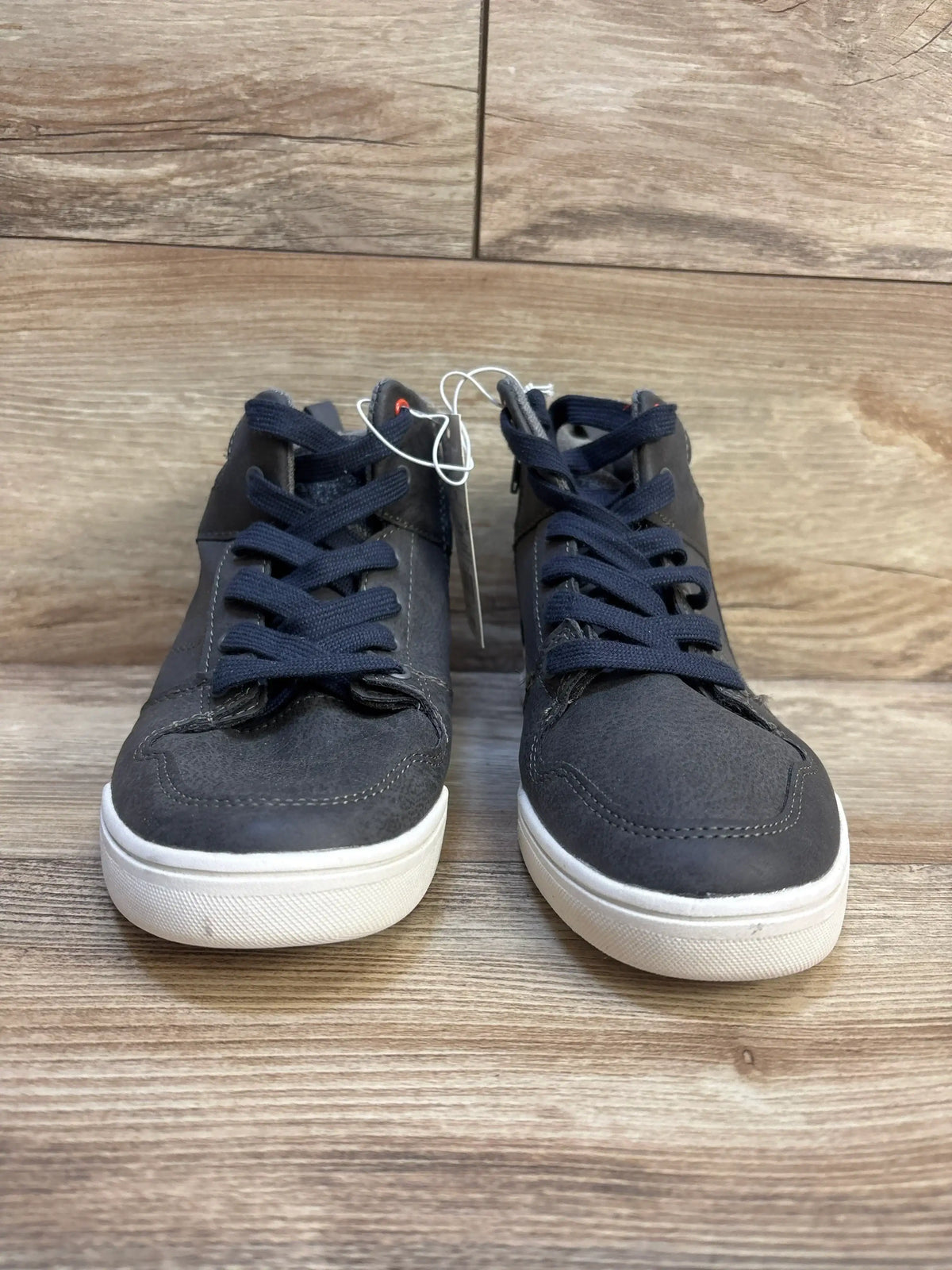 Front view of Art Class Geoff kids’ high-top sneakers, grey upper with navy laces and white rubber soles on wood background