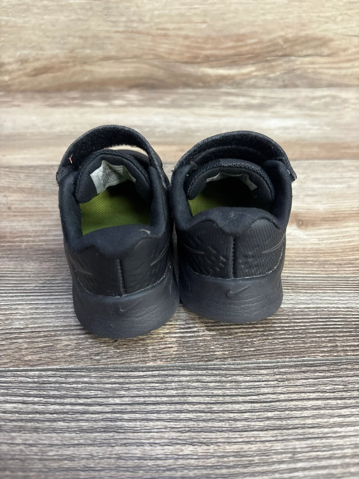Rear view of black Nike Star Runner 2 TDV toddler sneakers size 4C showing Velcro straps, green insoles on wood background