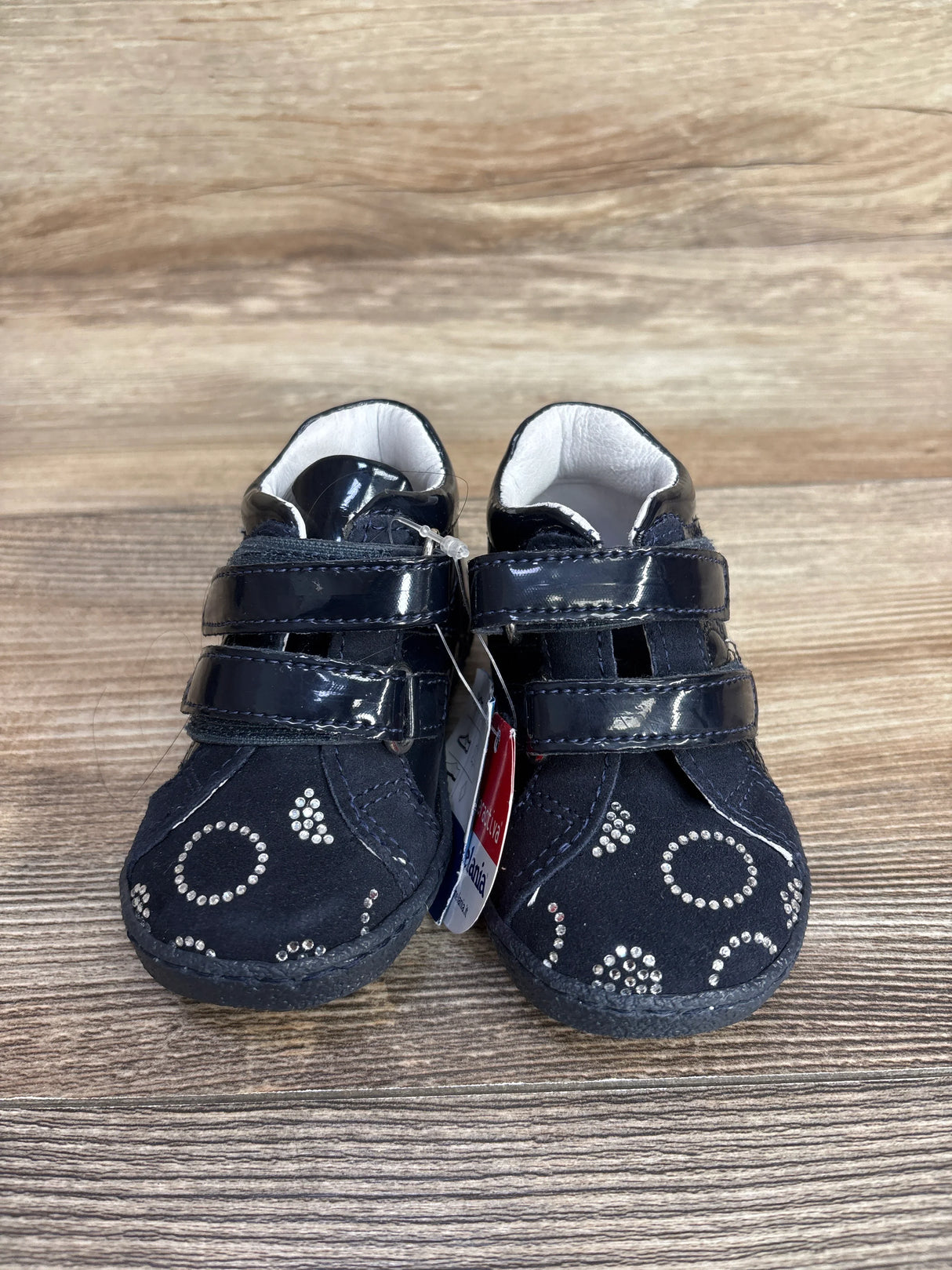 Pair of navy blue baby shoes with shiny straps and silver rhinestone circle patterns on a wooden surface