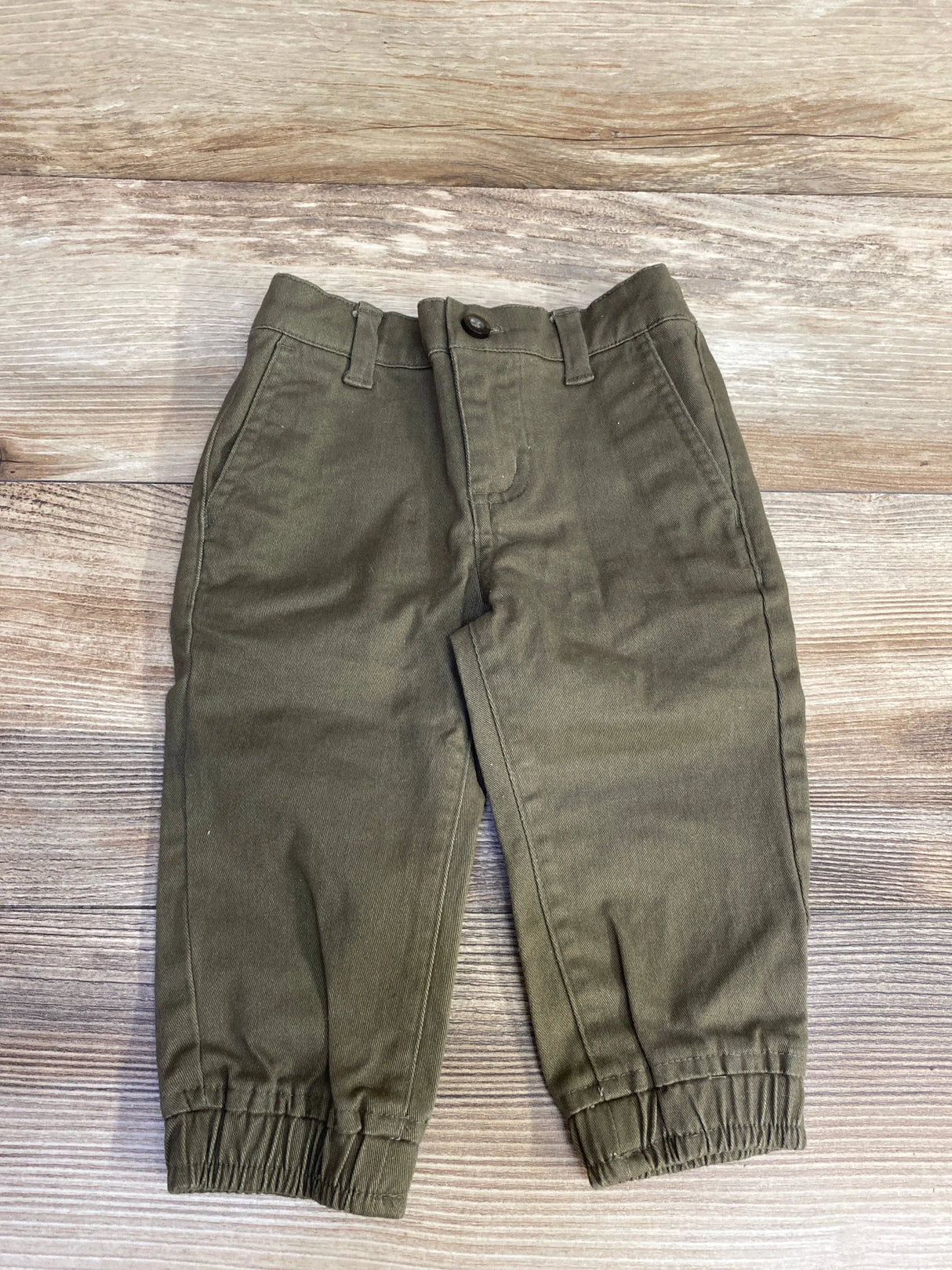 Olive green toddler pants with elastic cuffs on wooden background