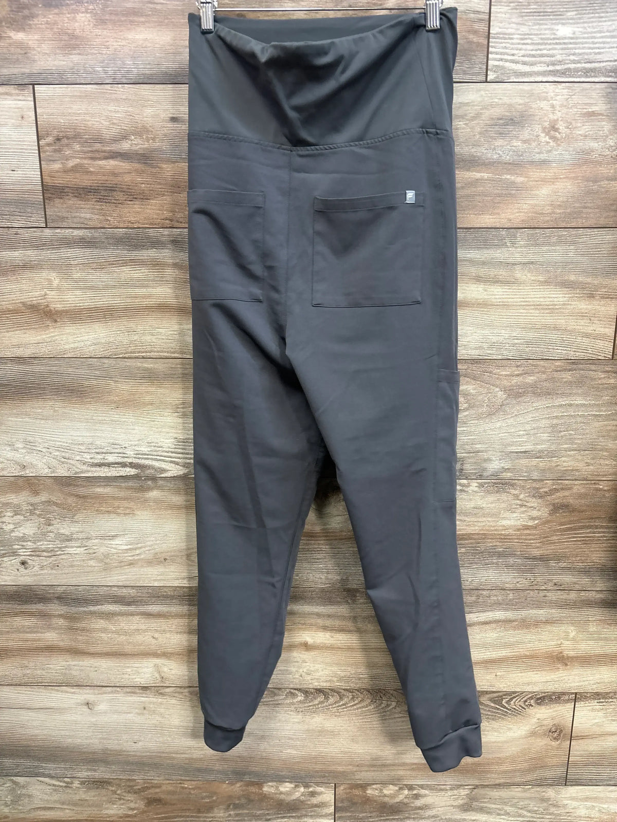 Back view of Fabletics maternity scrub joggers with high rise panel, patch pockets and cuffed ankles on wood wall