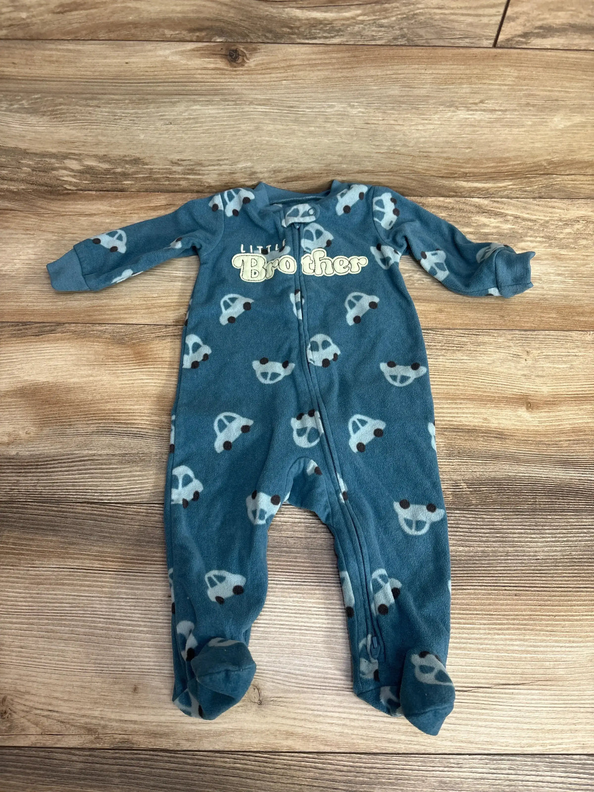 Top-down view of teal Carter’s footed blanket sleeper showcasing car print and Little Brother chest text on wooden floor