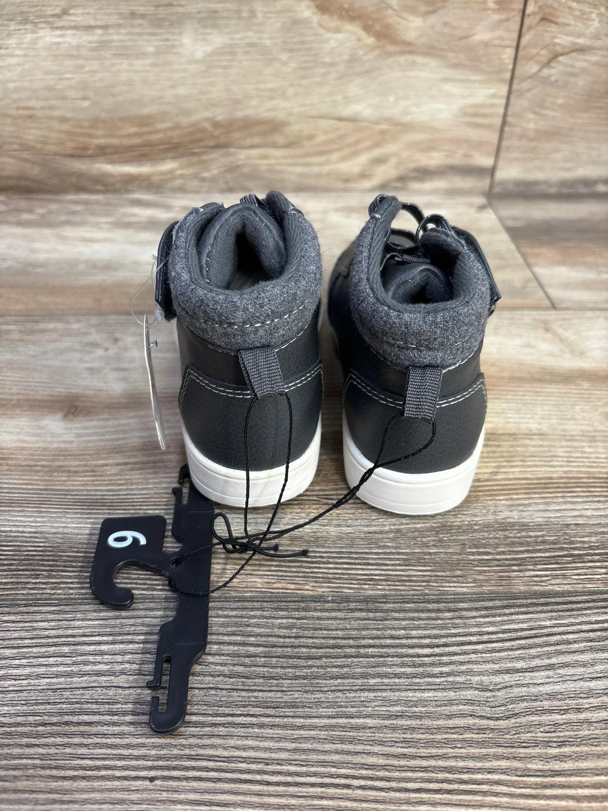 Back view of black and gray toddler sneakers with white soles on wooden floor, size 6 tag attached
