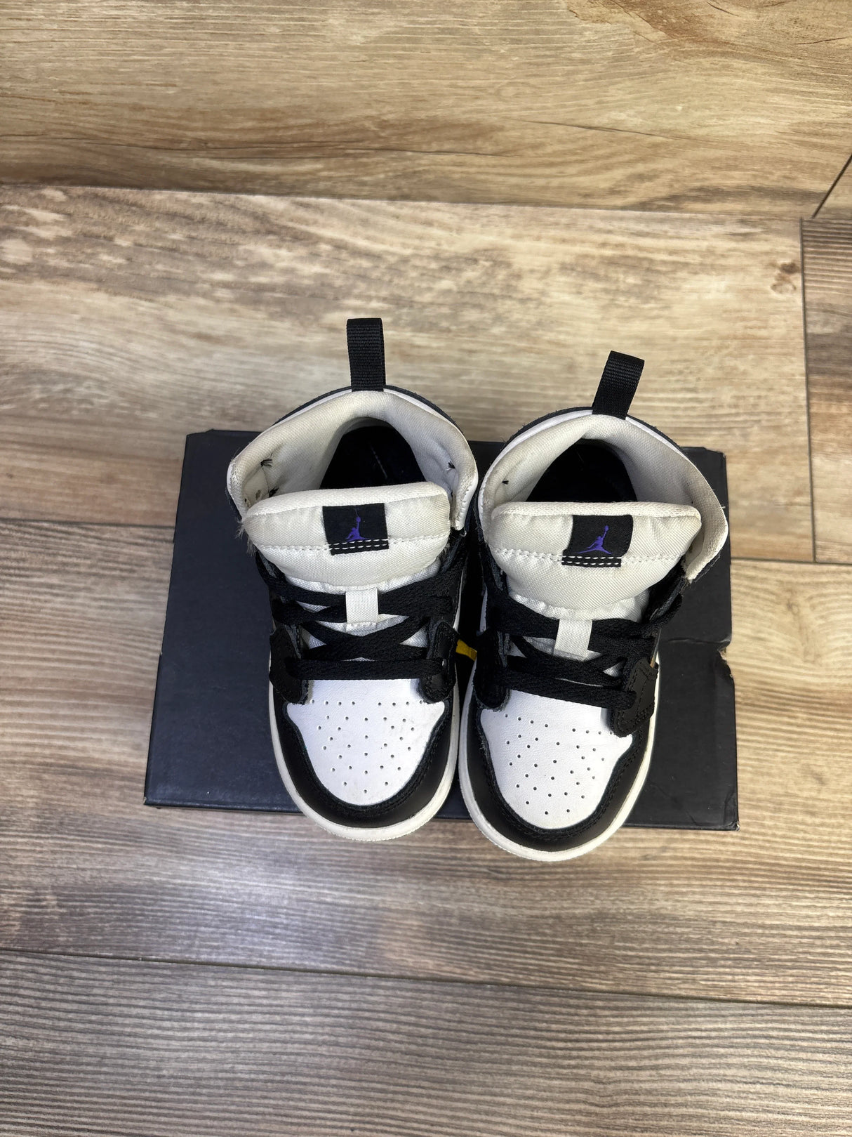 Overhead of Jordan 1 Mid Hologram toddler sneakers, white toe, black panels, purple Jumpman on tongue, on a black box
