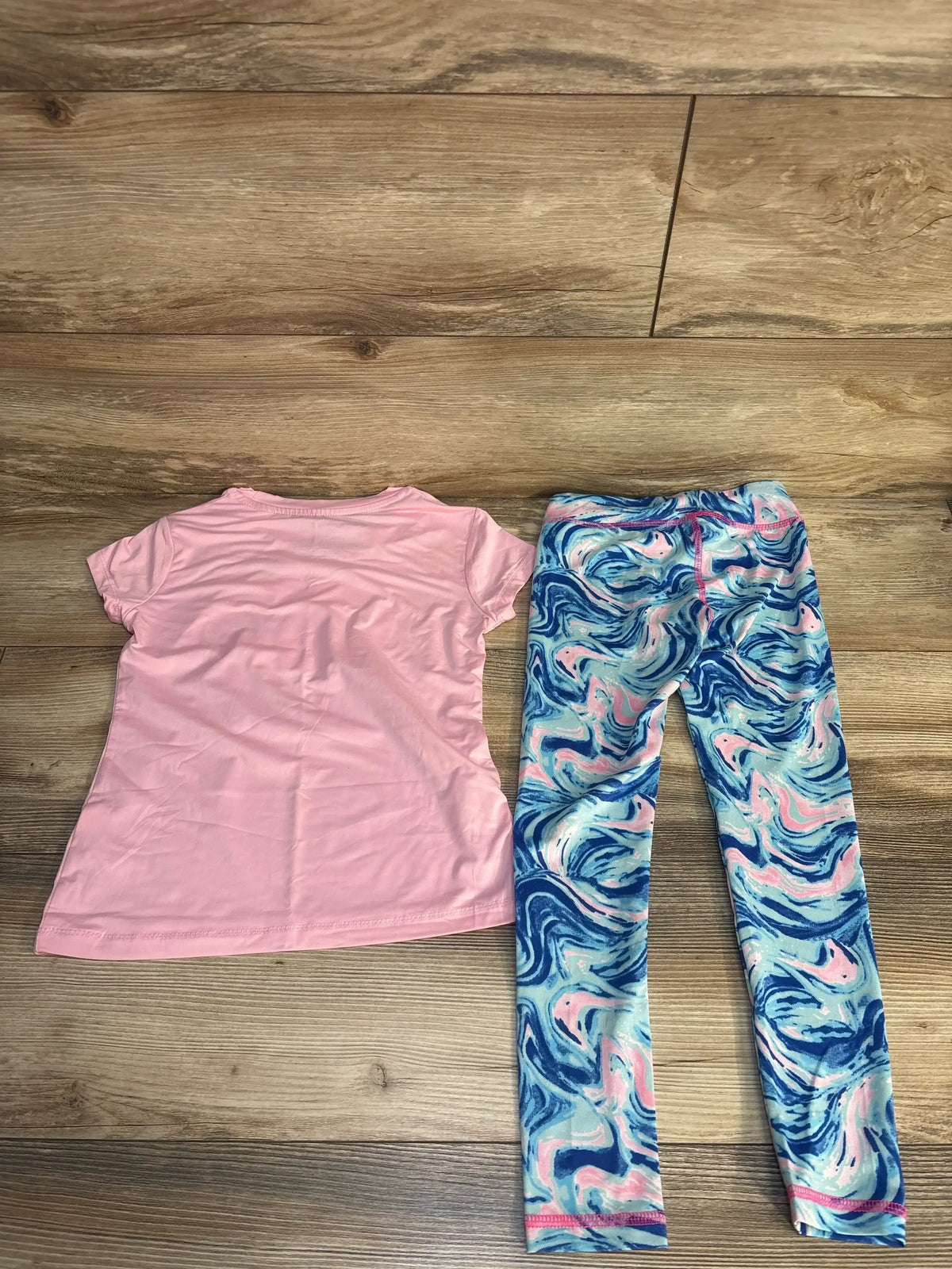 Flat lay of pink short sleeve shirt and blue swirl print leggings for kids on wood plank floor
