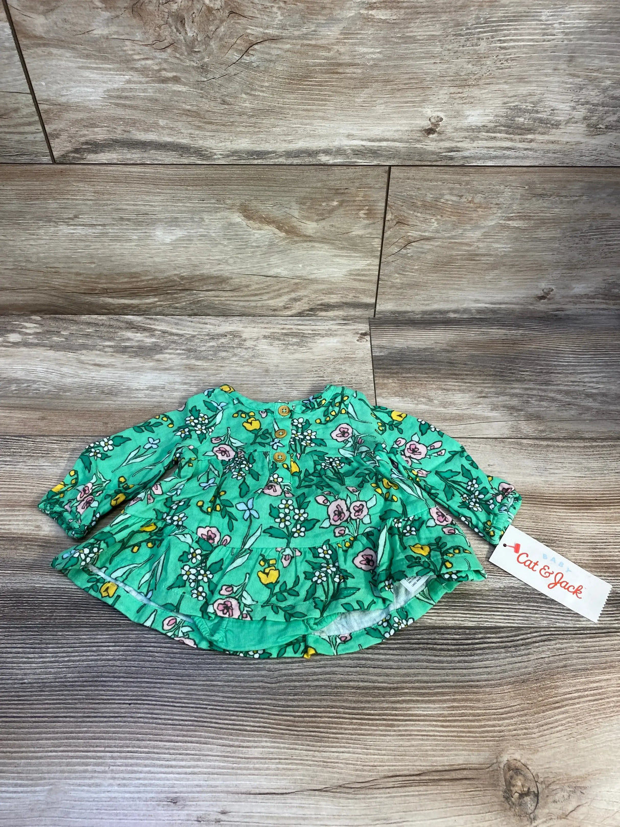 Flat-lay of Cat & Jack newborn green floral henley dress showing front buttons and ruffled skirt on wood background