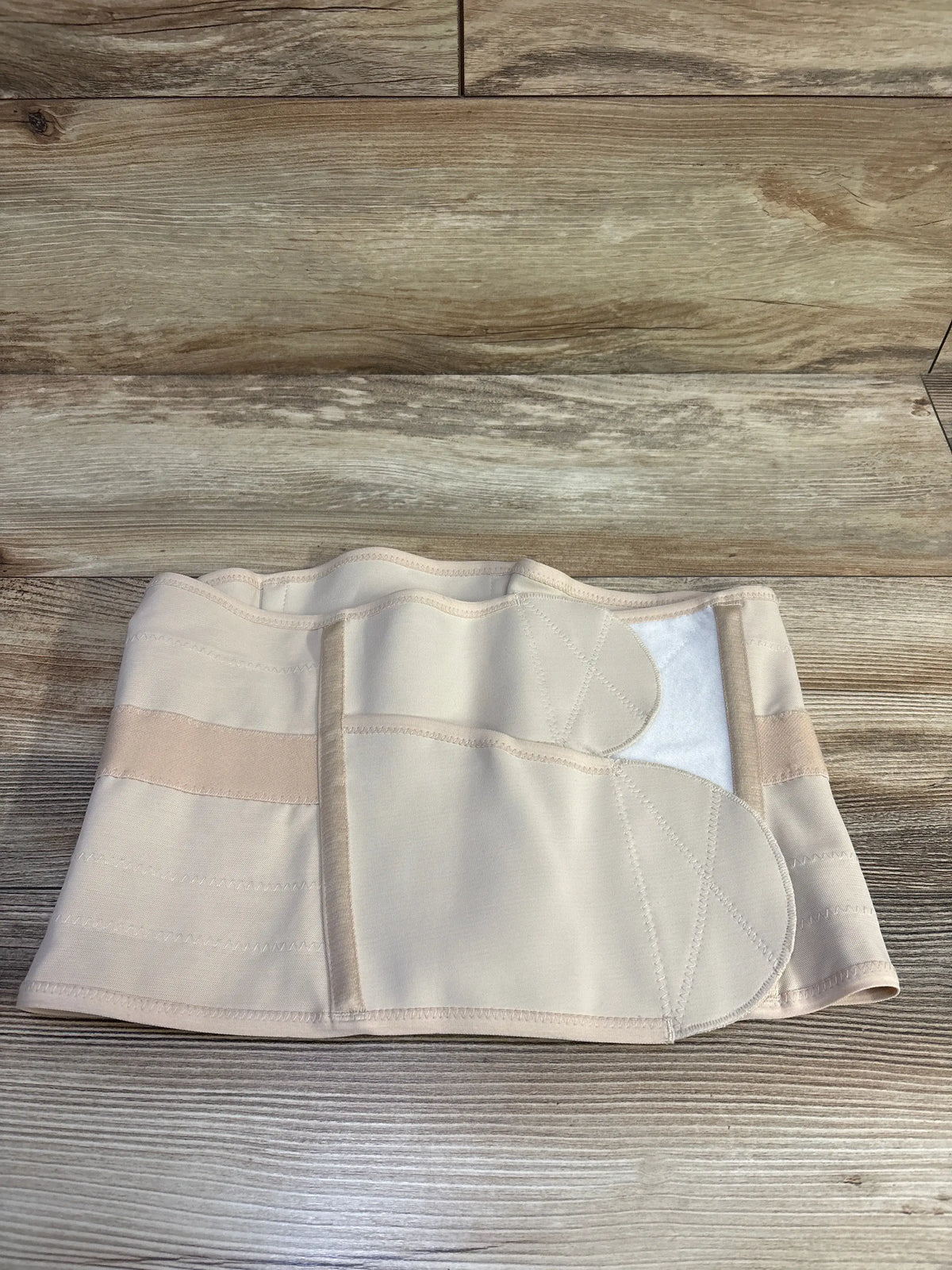 Beige Belly Bandit Luxe Postpartum Belly Wrap in size medium laid flat on a wooden surface.
