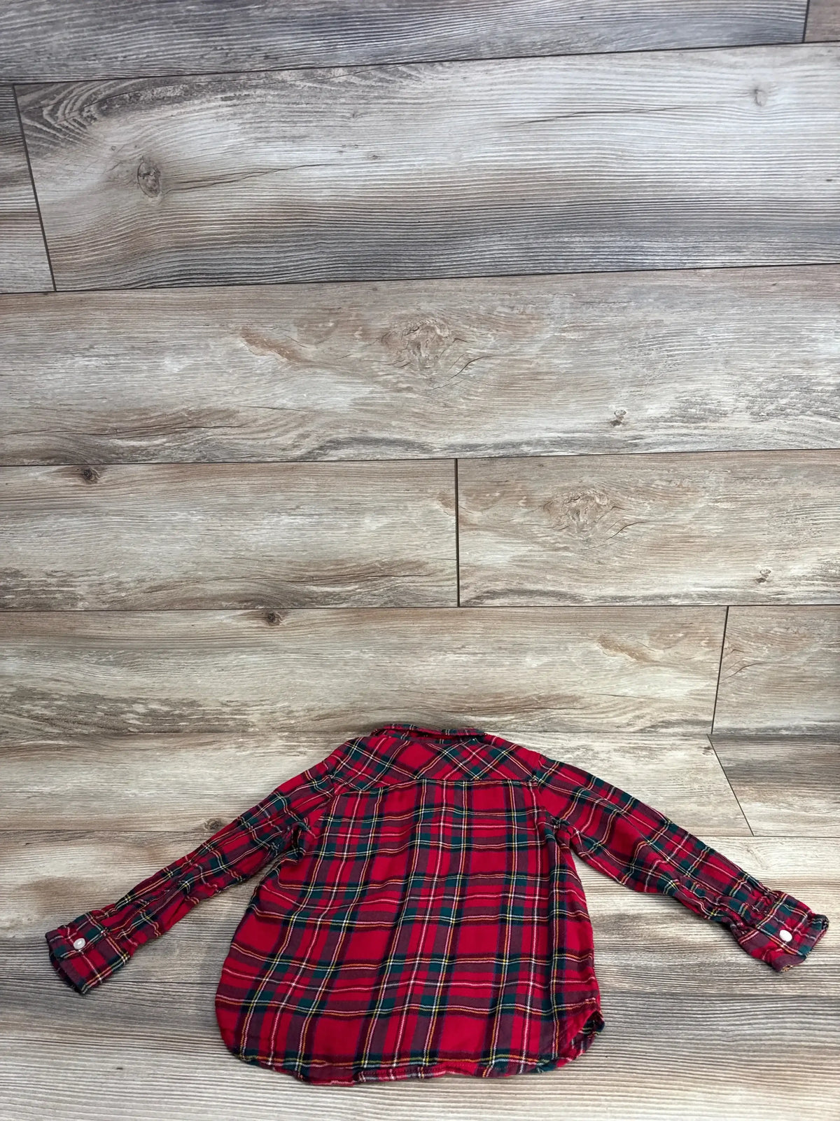 Back view of H&M red plaid button-up toddler shirt (size 5T) showing yoke and long sleeves laid flat on wood background