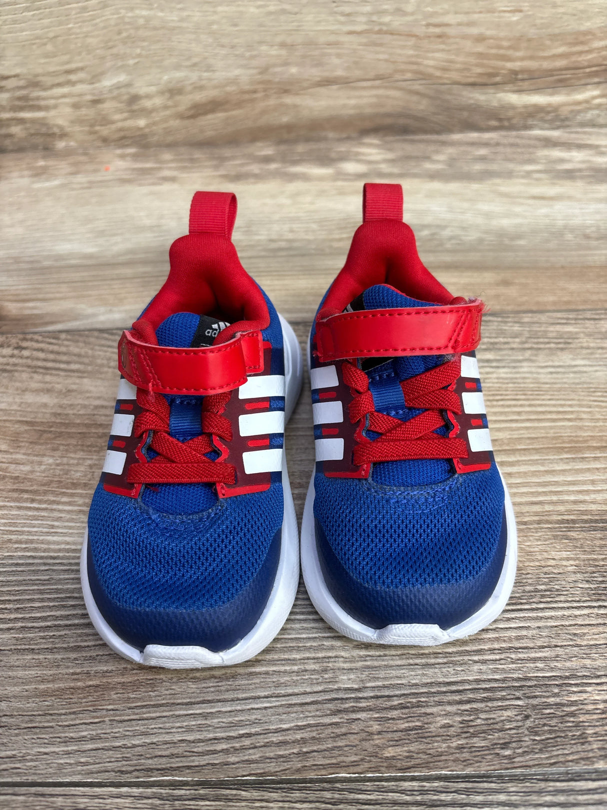 Blue and red toddler sneakers with white stripes and velcro straps on wooden floor