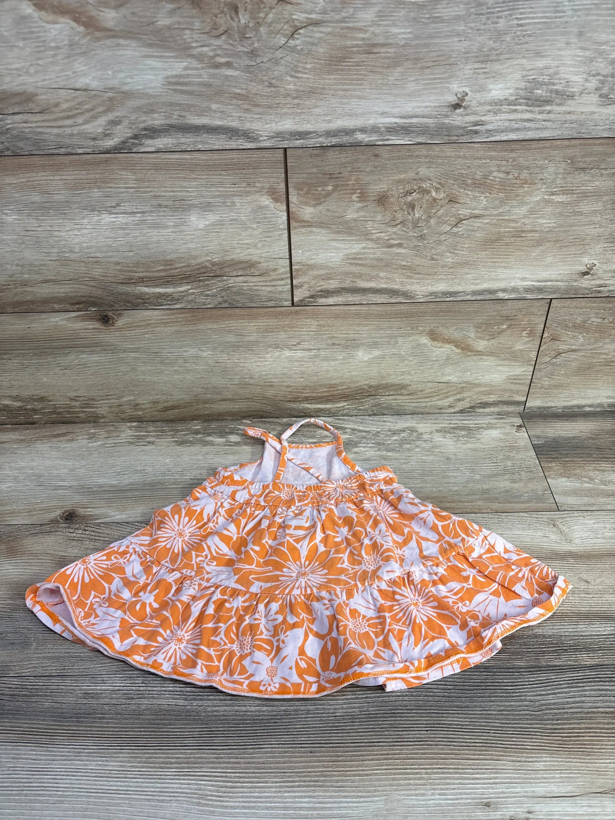 Front view of Cat & Jack tank dress showcasing orange-and-white floral print, thin straps, gathered waist, and flared skirt on wood flooring
