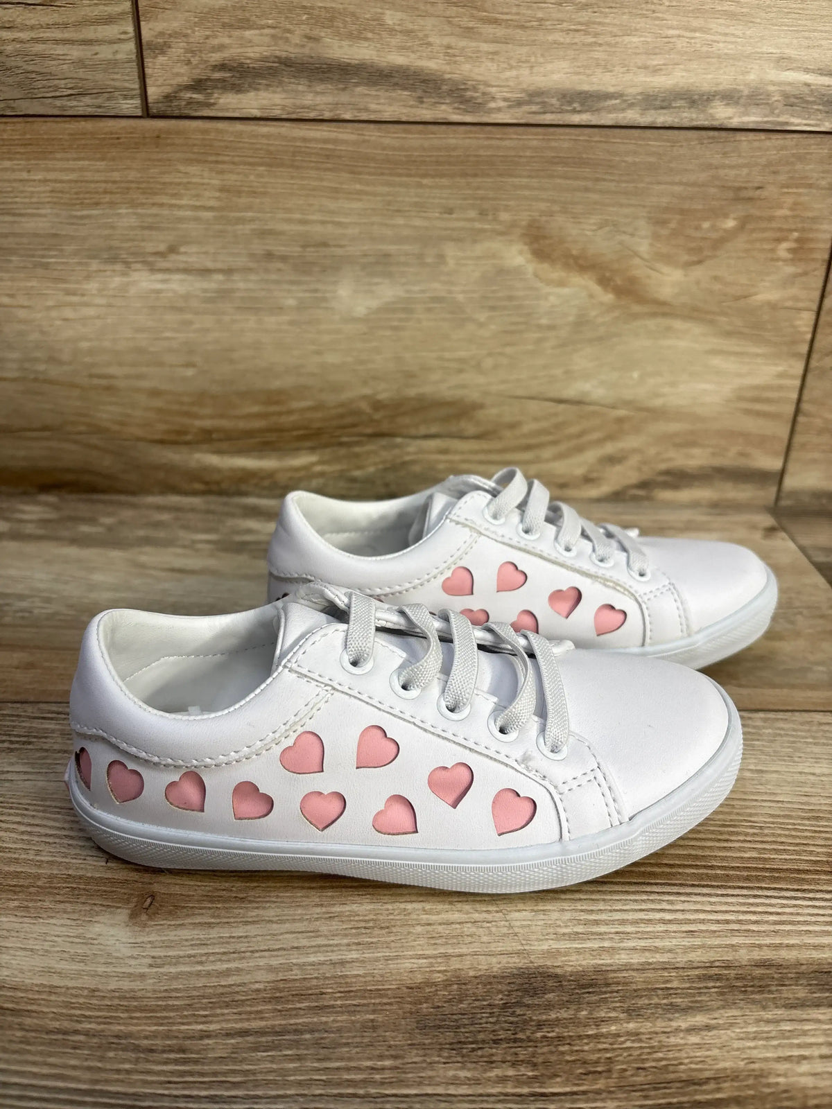 Side view of Janie & Jack heart sneakers in white, showcasing pink heart details and bungee laces on a wood floor