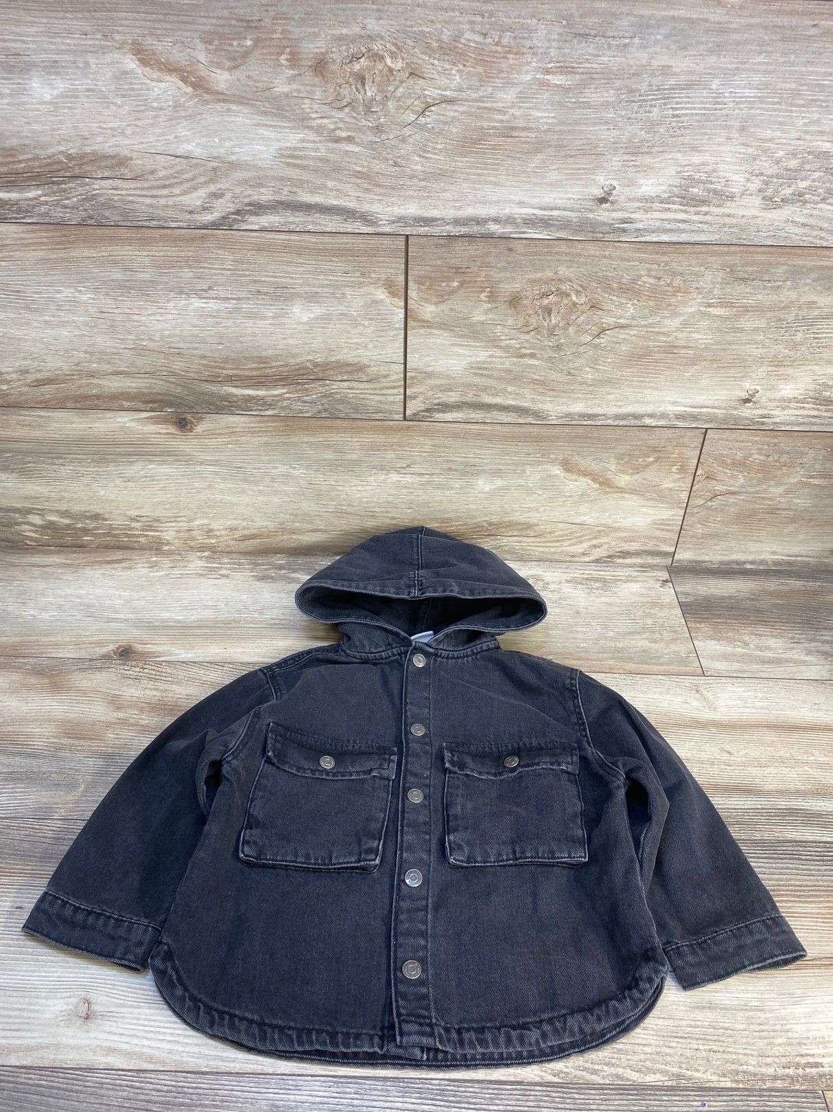 Black denim hooded kids jacket with front buttons and chest pockets on wood floor