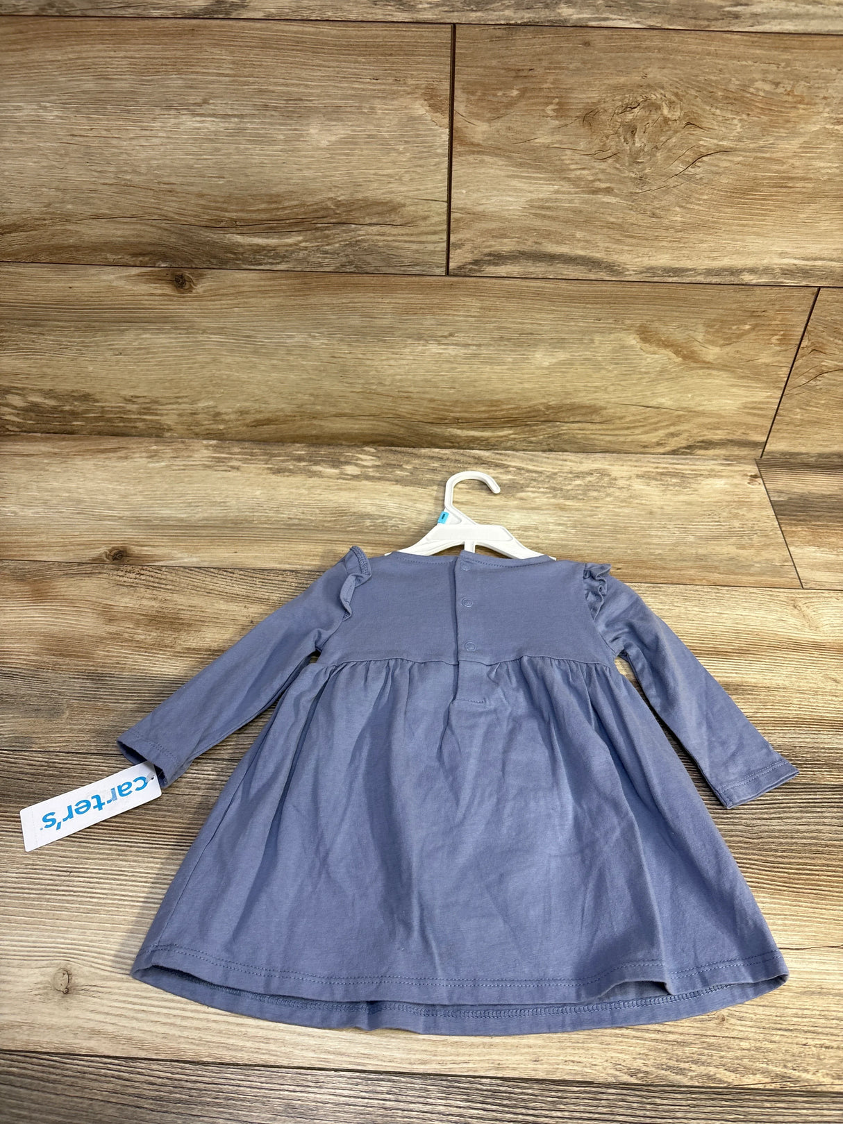 Back view flat lay of Carter’s blue long-sleeve lace dress and bloomers set showcasing ruffle shoulder detail on wood floor background