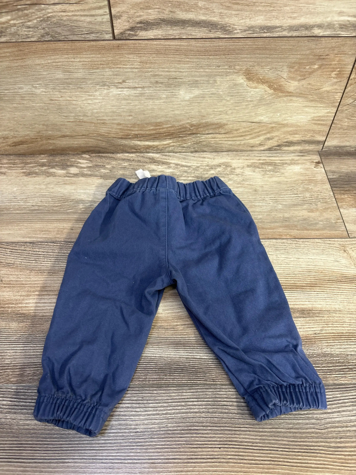 Front flat lay of baby jogger pants showcasing elastic waistband and gathered cuffs, size 6 months, on wood floor background