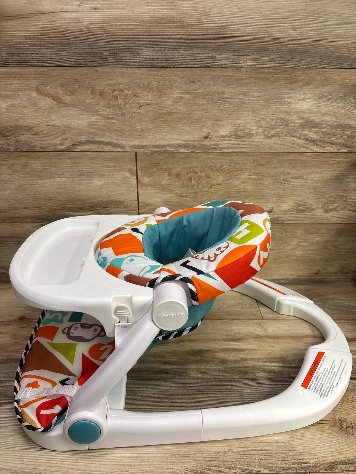 Angled view of Fisher-Price Deluxe Kick & Play Sit-Me-Up Floor Seat showcasing padded seat, tray, and kick mat on wood flooring