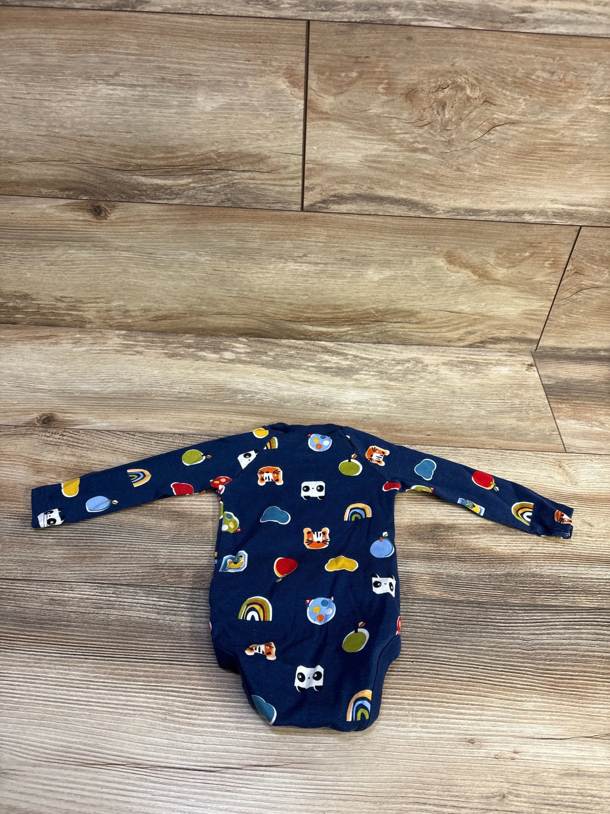 Flat lay of Okie Dokie navy long-sleeve bodysuit showing multicolor animal, rainbow, and balloon print on wood floor