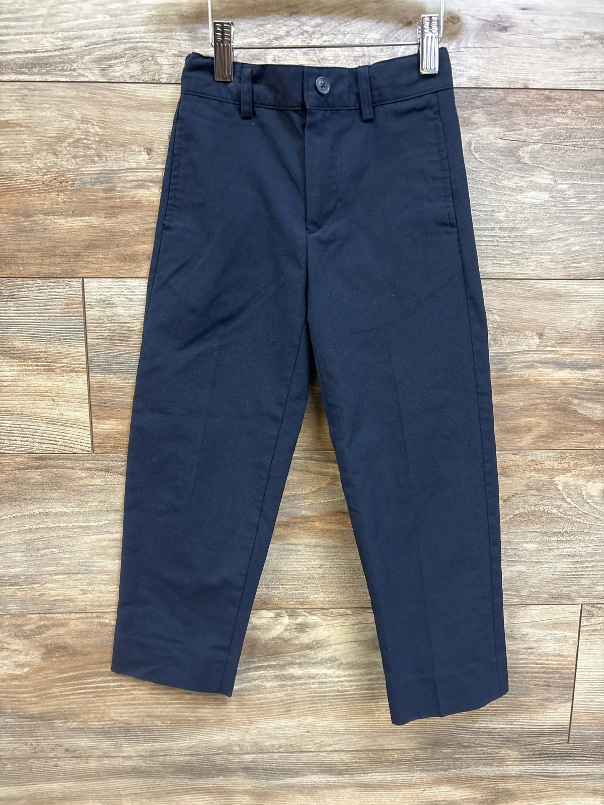 Front view of Cat and Jack navy straight-fit uniform pants with front crease, button waist and belt loops on wood background