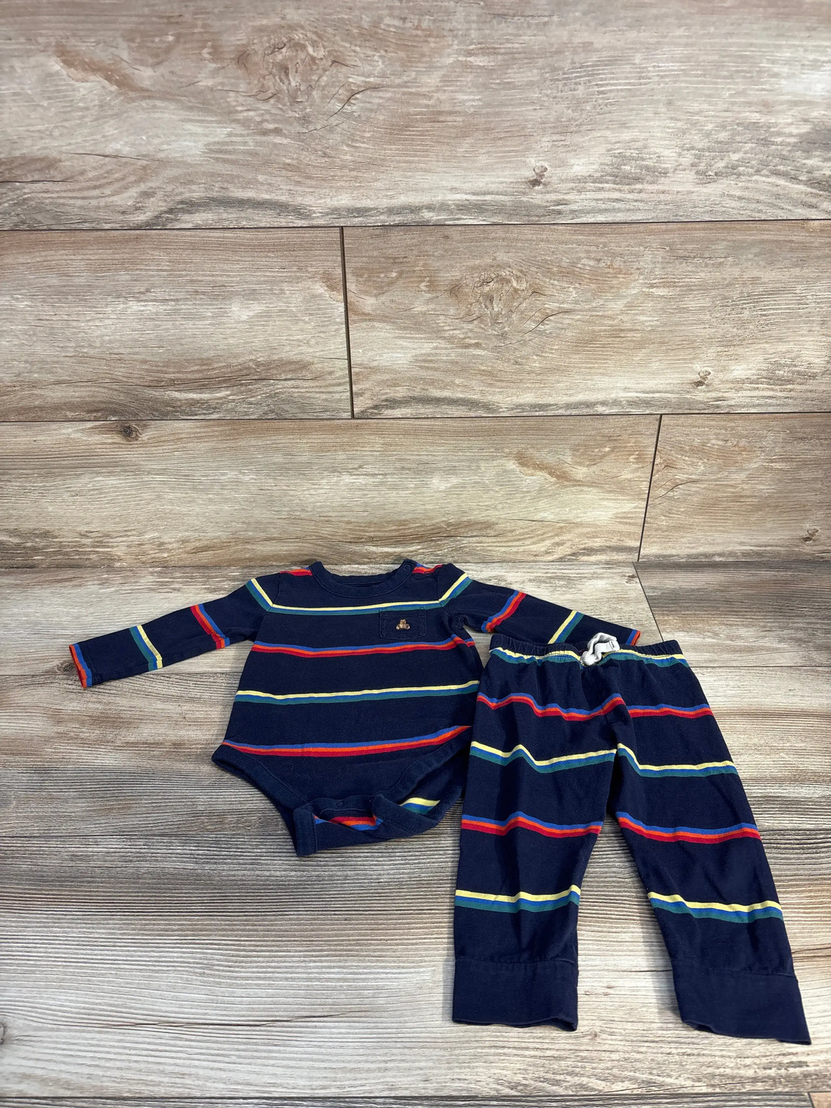 Top view of Baby Gap 2pc striped bodysuit and pants set showcasing navy fabric with multicolor stripes on a wood-look floor