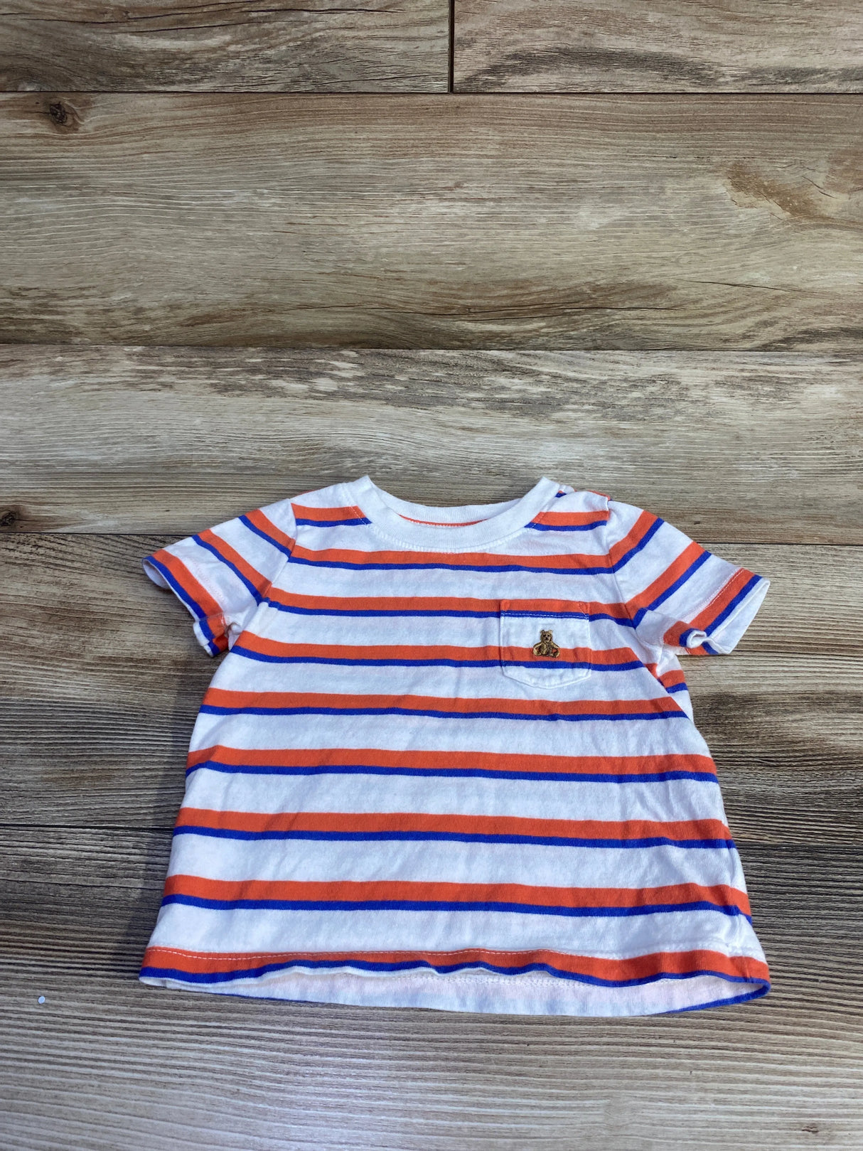 Front view of Baby Gap striped short-sleeve pocket shirt showing orange and blue stripes and small embroidered bear on a wood background