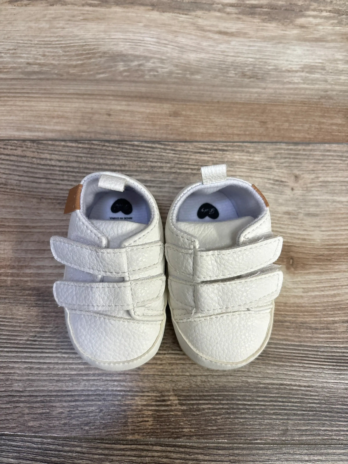 Top view of white Myggpp baby sneakers with double velcro straps and pebbled leather on wood floor